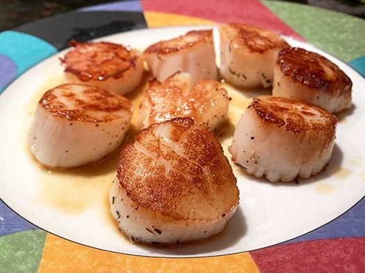 Seared scallops on a white plate with a colorful tablecloth