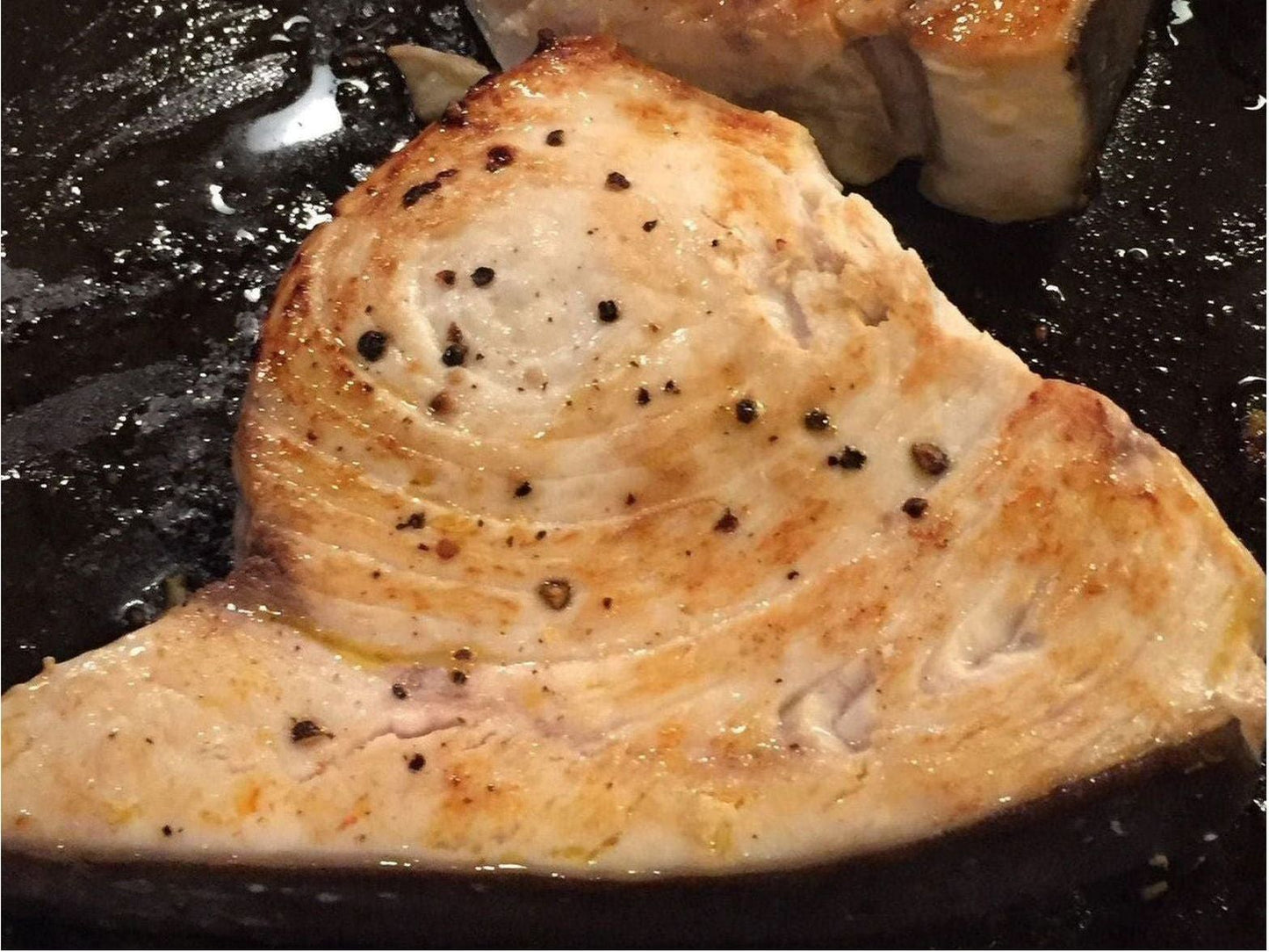 Seared fish fillet with pepper on a black surface