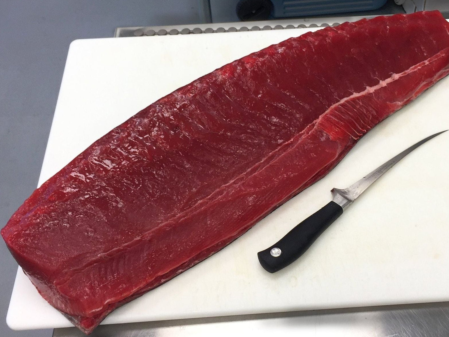 A whole, fresh yellowfin tuna on a cutting board with a knife next to it, indicating it is ready to be cut and prepared.