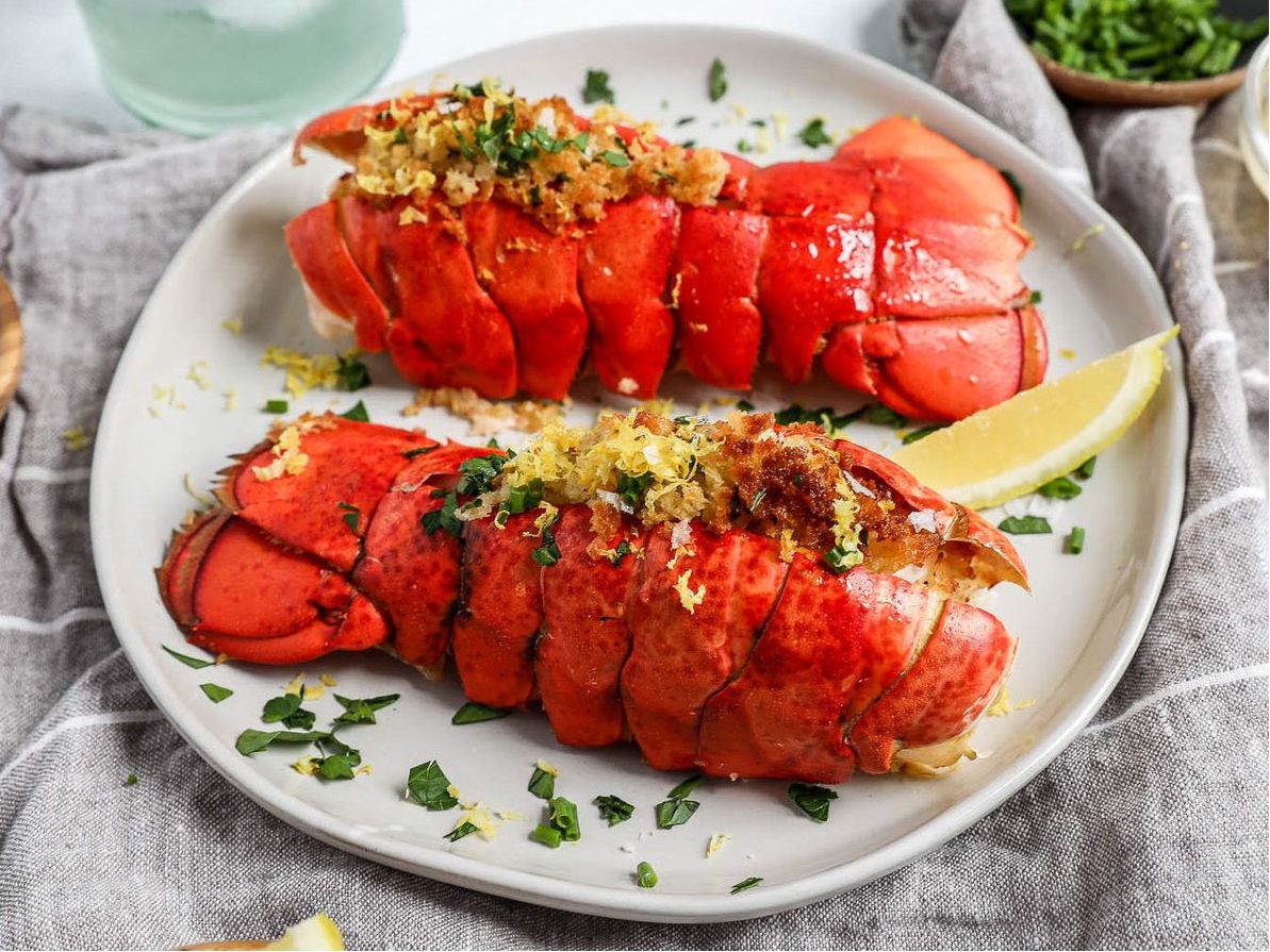 A plate with two cooked lobster tails garnished with herbs and lemon.
